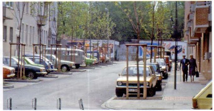 Улица в квартальной застройке с парковками, разделенными клумбами с деревьями